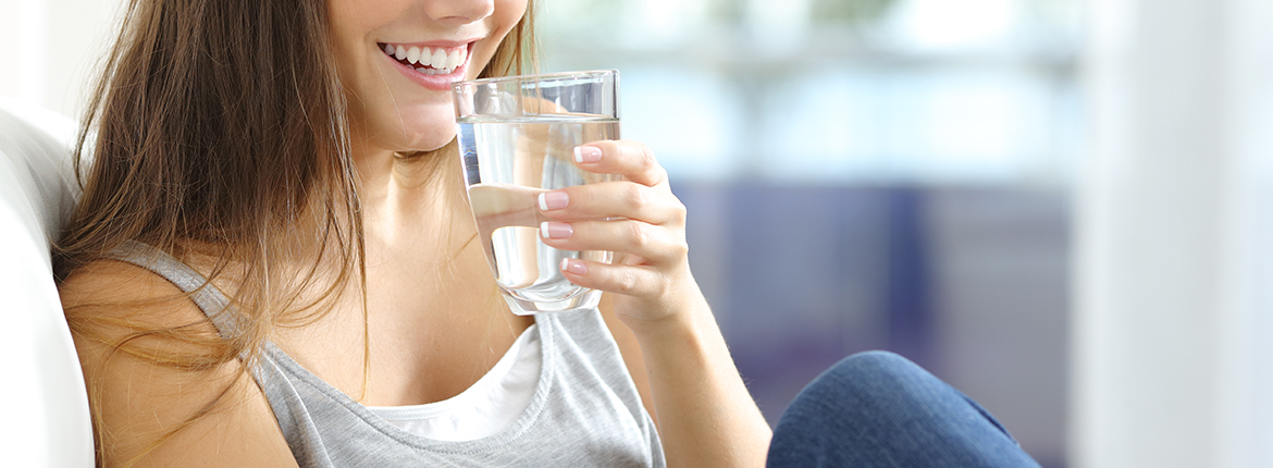 Lächelnde Frau kurz davor aus ihrem Wasserglas zu trinken, um Halsschmerzen zu lindern.
